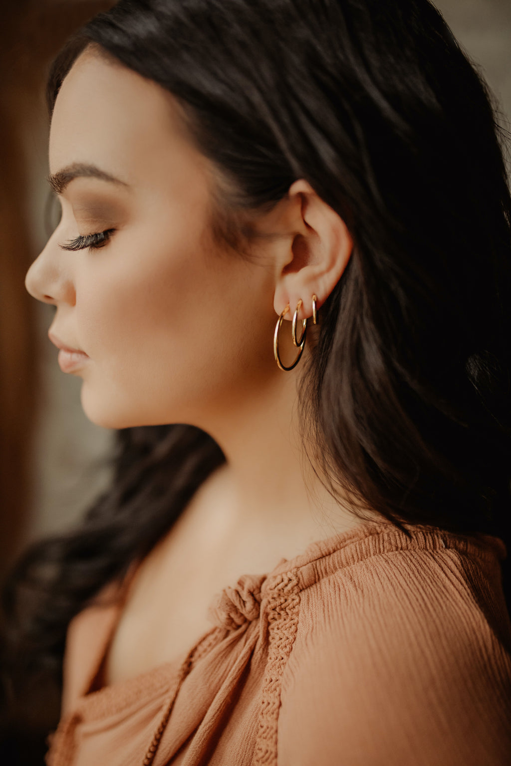 Woman standing sideways wearing large gold hoop earrings and smaller hoops as well.