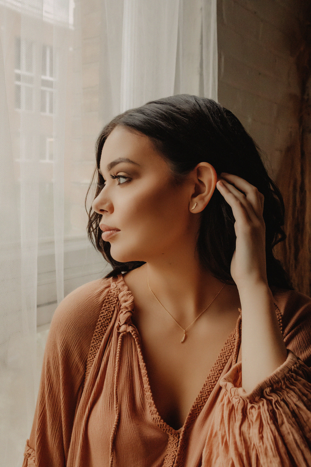 Woman wearing gold feather earrings and necklace.