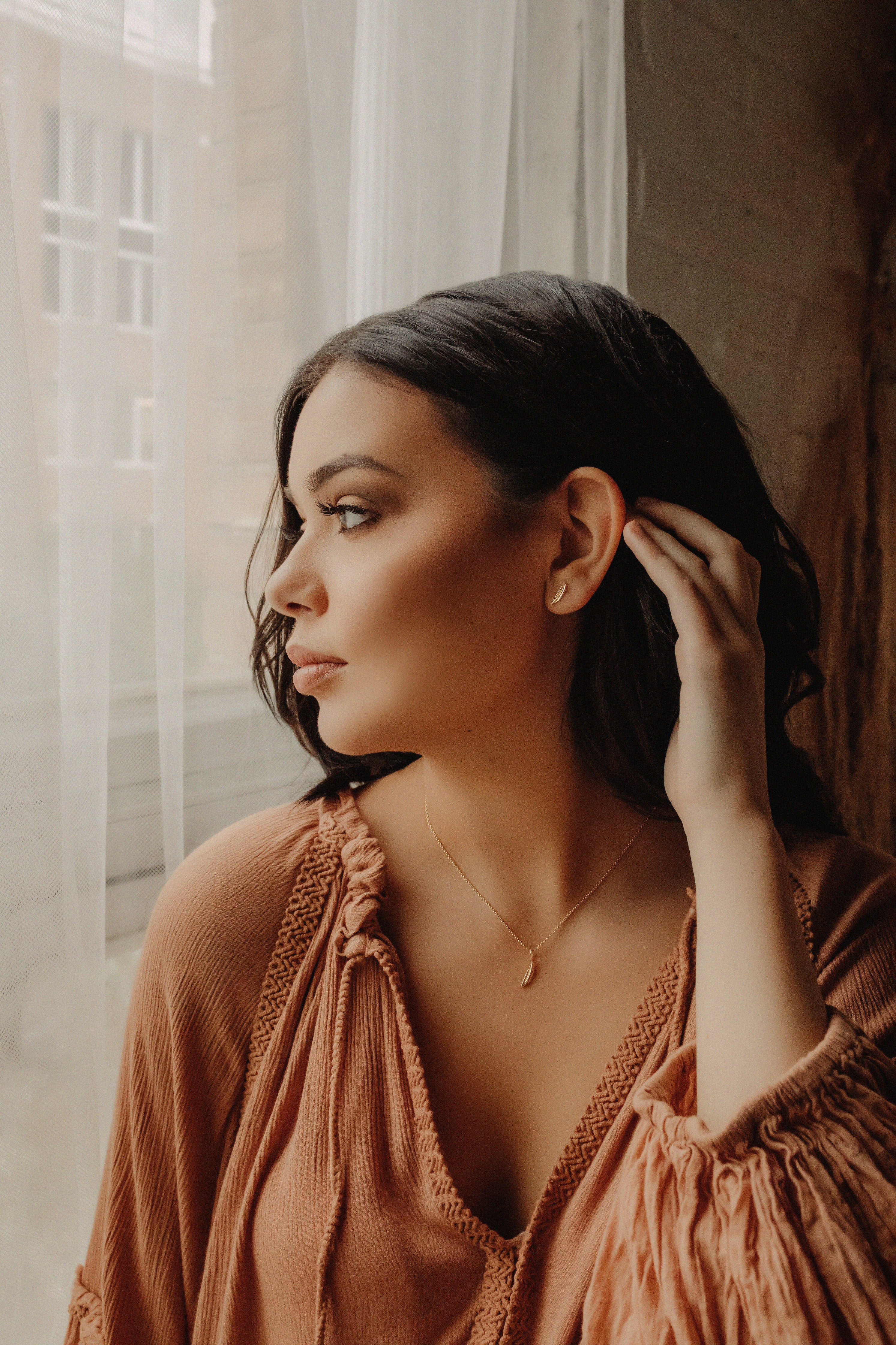 Woman wearing gold feather earrings and necklace.